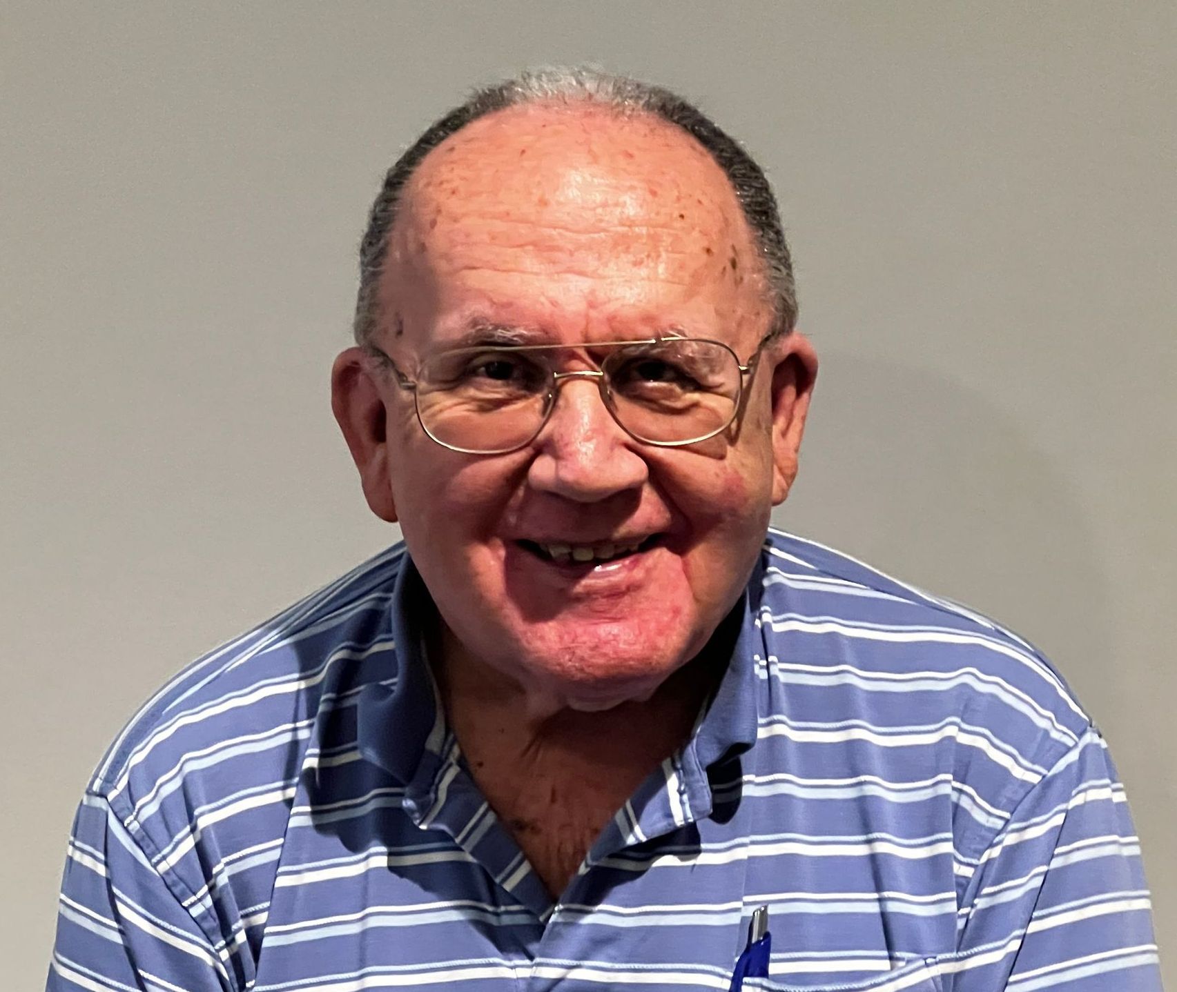A man wearing glasses and a striped shirt smiles for the camera