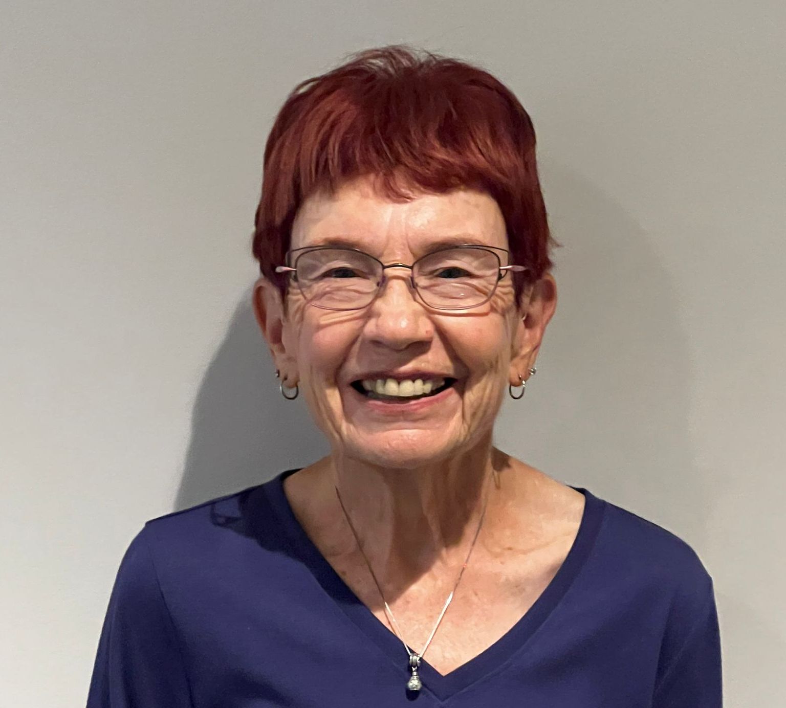 A woman wearing glasses and a blue shirt is smiling for the camera.