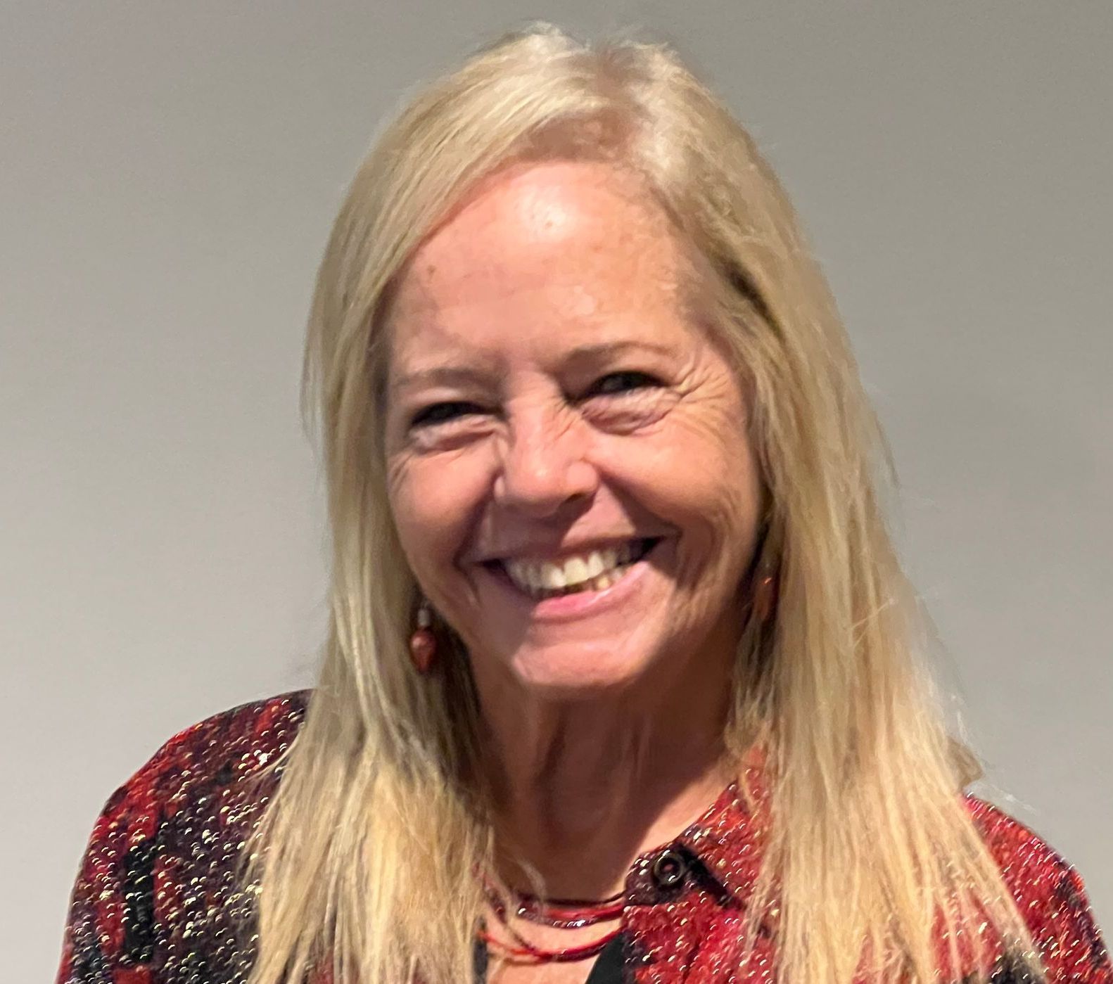 A woman with long blonde hair is smiling and wearing a red and black shirt.