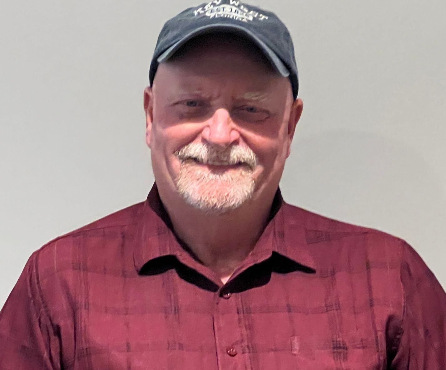A man wearing a hat and a red shirt is standing in front of a white wall.