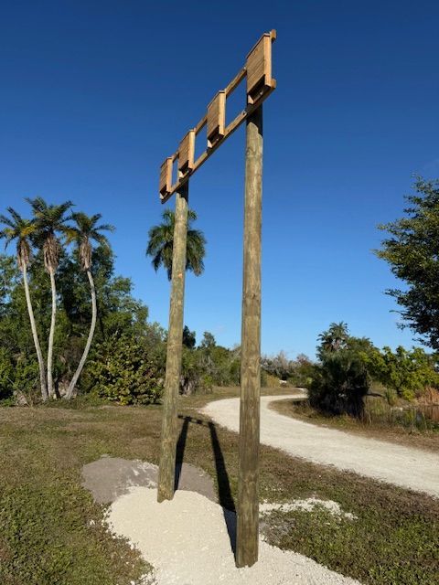 Wooden structure with openings, on a path with a palm tree background.