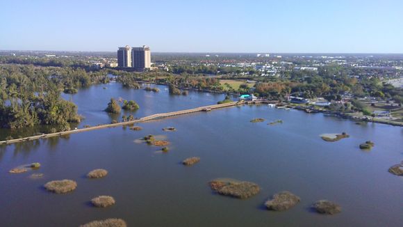 Aerial view of a body of water with small islands, a walkway, and a distant building under a clear sky.