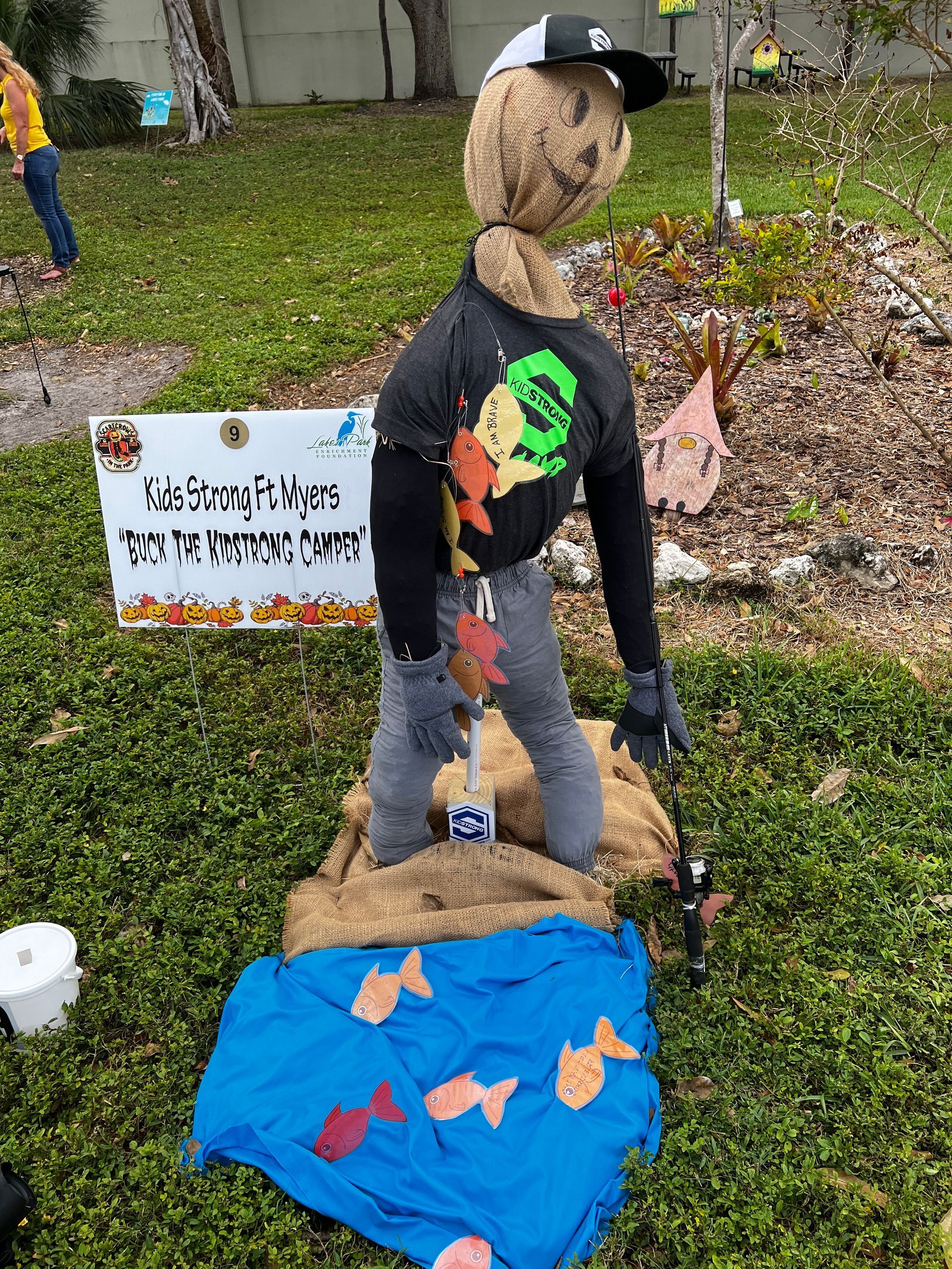 A scarecrow is standing in the grass next to a sign.