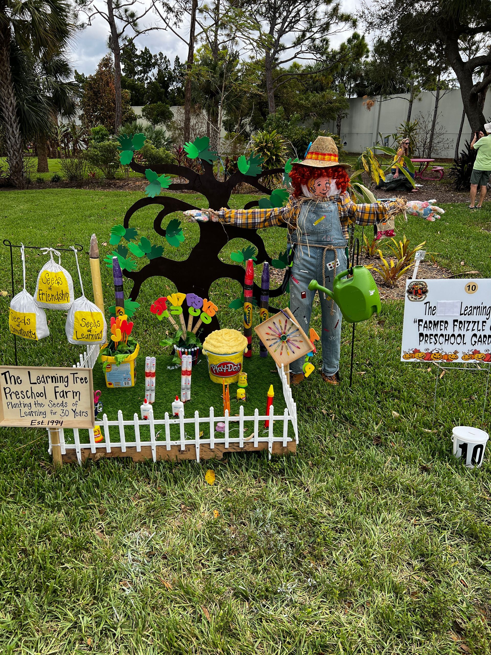 A scarecrow is holding a watering can in a garden.