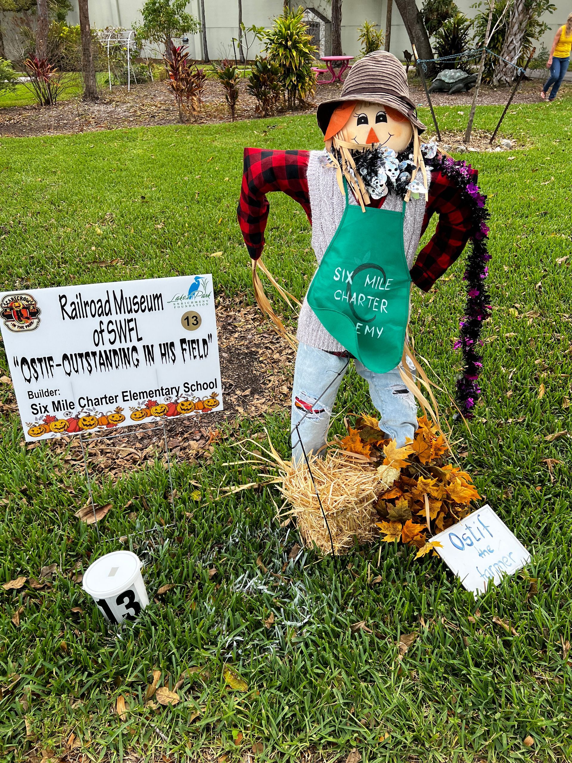 A scarecrow is standing in the grass next to a sign.