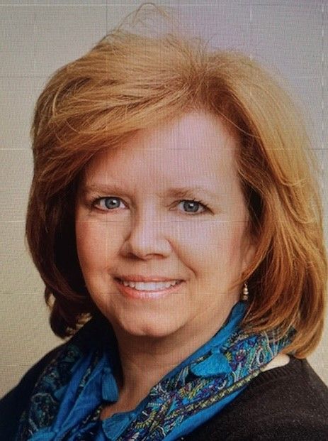 A woman with red hair and a blue scarf is smiling for the camera.