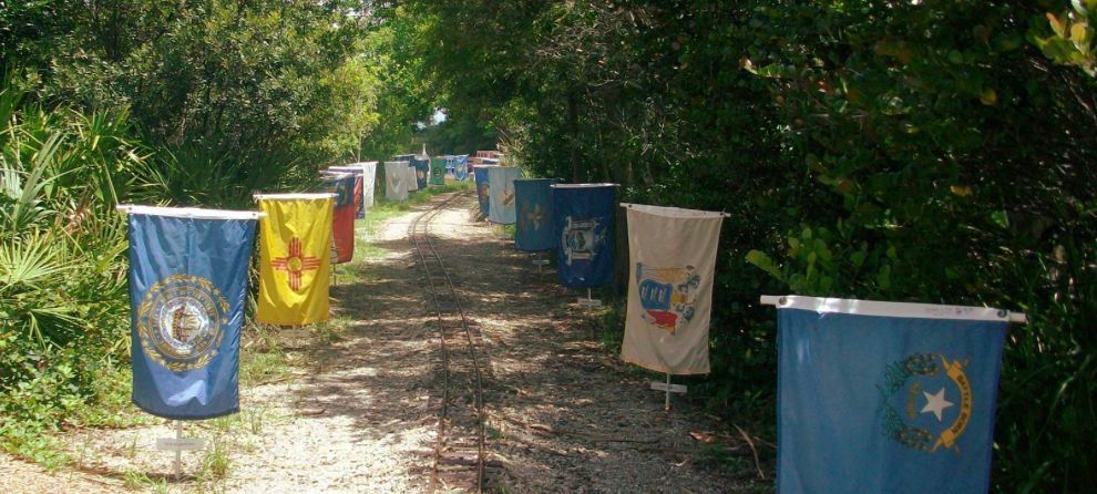 A row of flags hanging from trees on a dirt road.