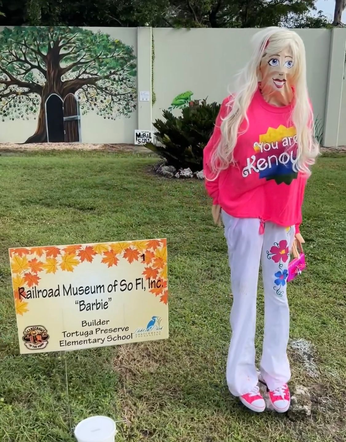 A barbie doll is standing in front of a sign that says railroad museum of so fl