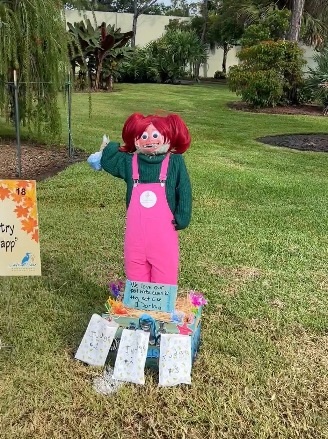 A scarecrow is standing in the grass next to a sign.