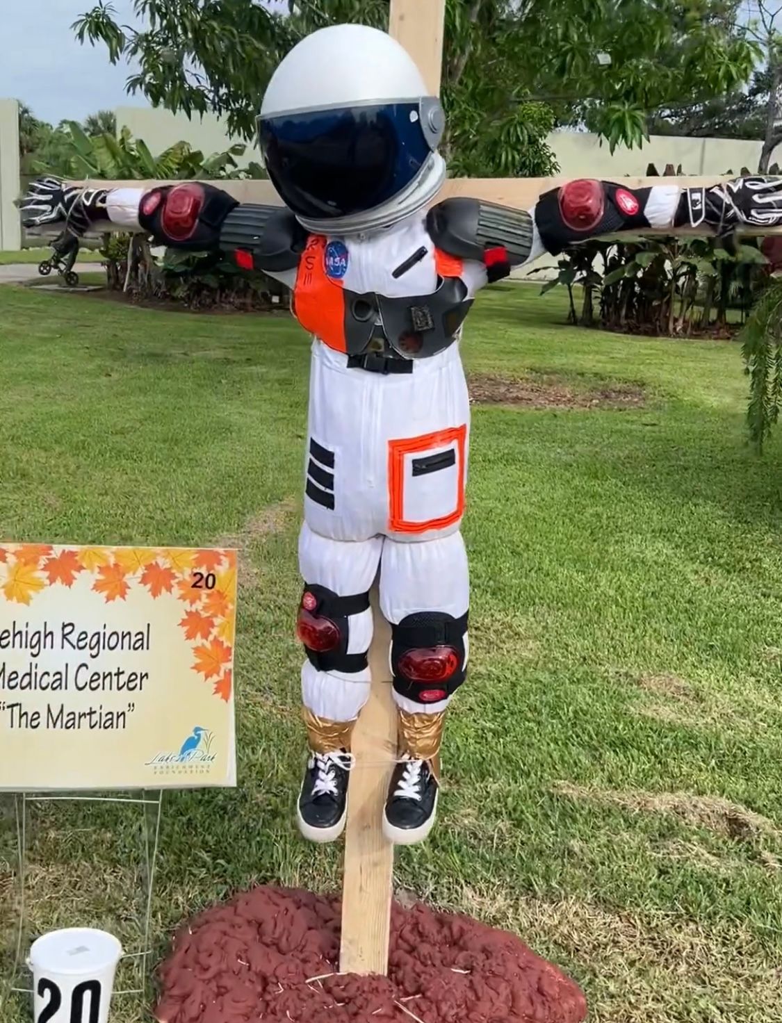A scarecrow dressed as an astronaut is hanging from a wooden post