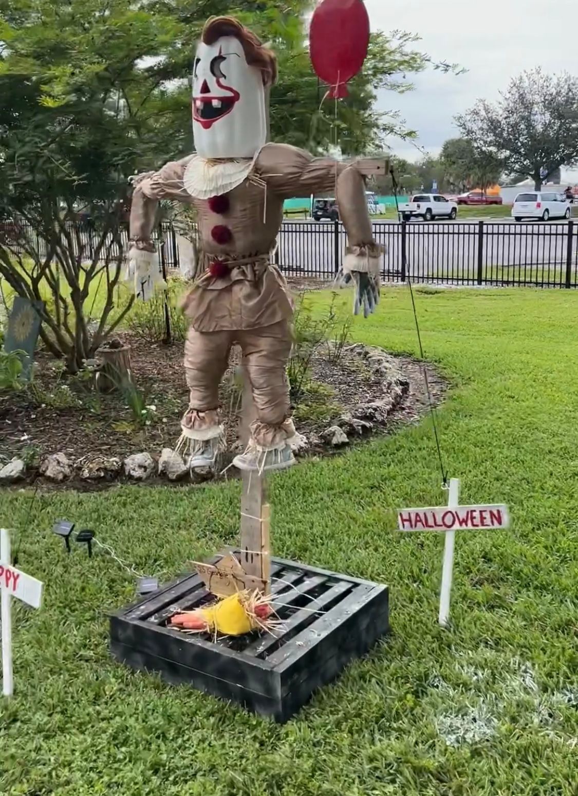 A scarecrow is holding a red balloon in his hand.