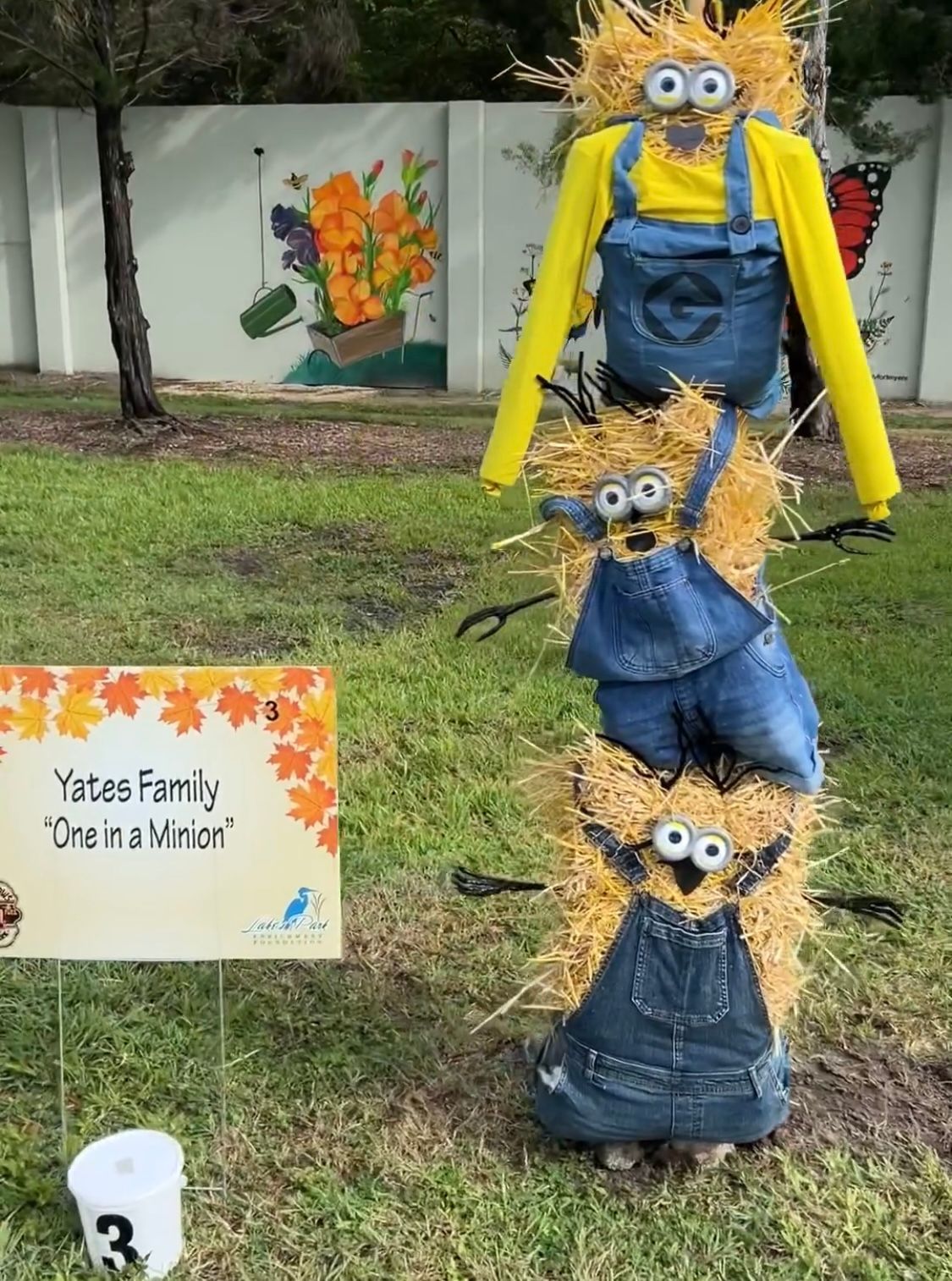 A scarecrow made out of straw is standing in the grass next to a sign.