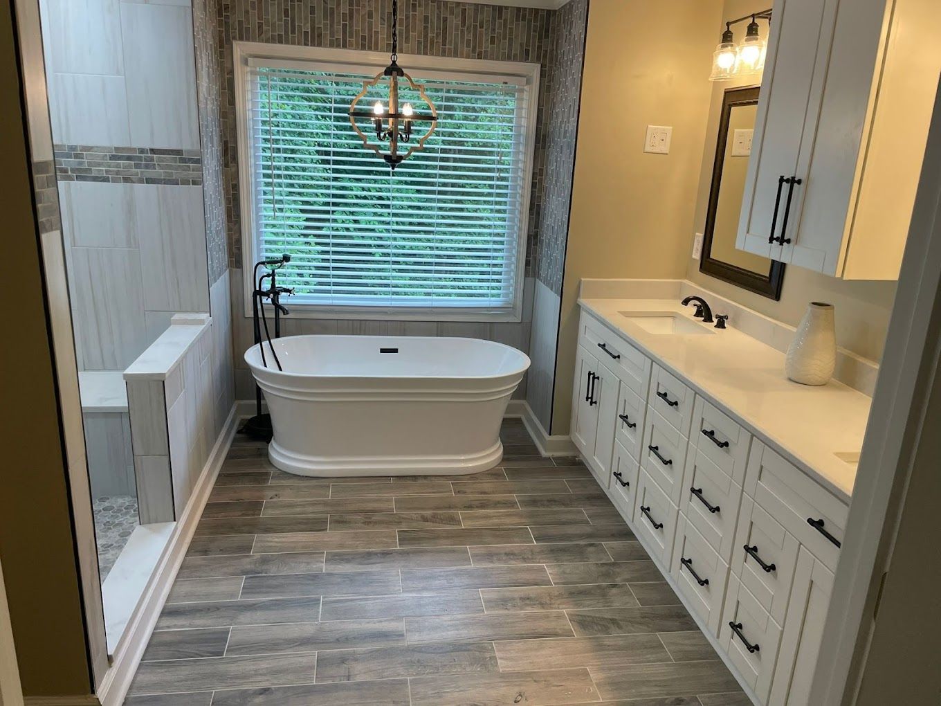 A bathroom with a tub , sink , mirror and window.