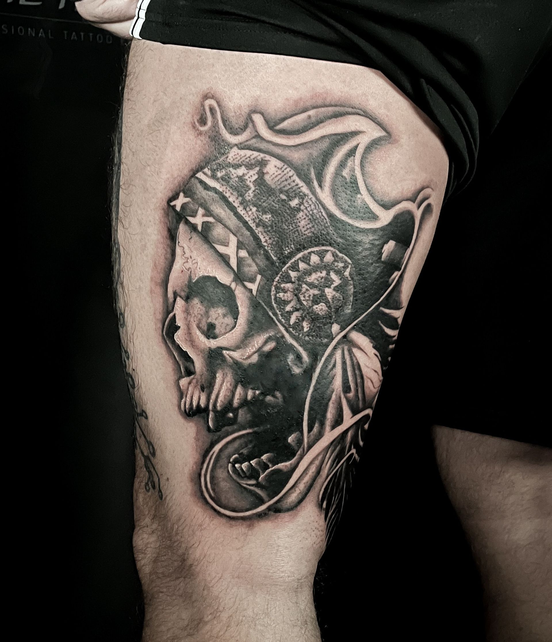 Black and gray skull tattoo on a thigh, featuring a headdress and intricate shading.