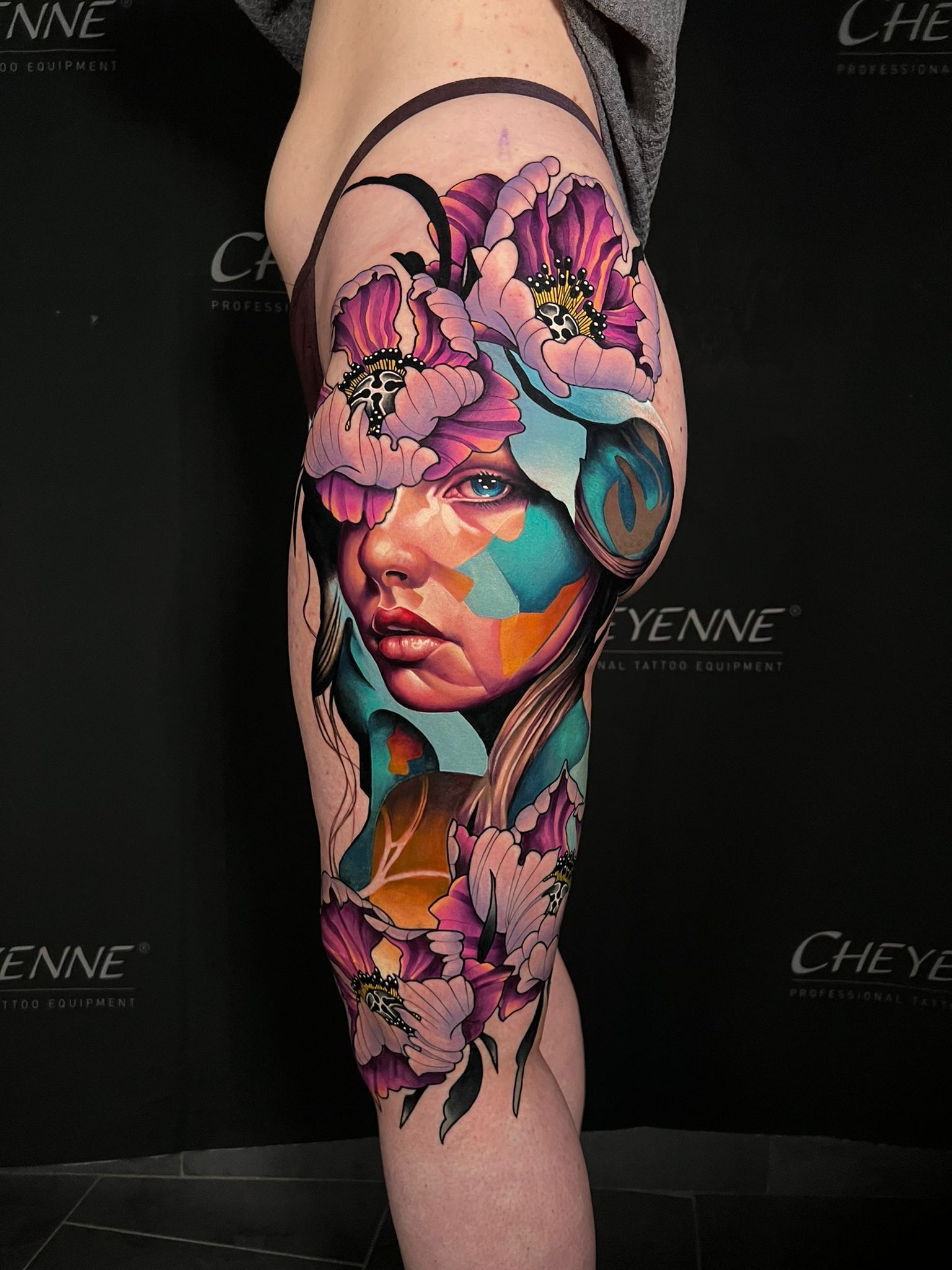 A colorful tattoo on a person's thigh depicts a woman's face, surrounded by flowers and abstract shapes.