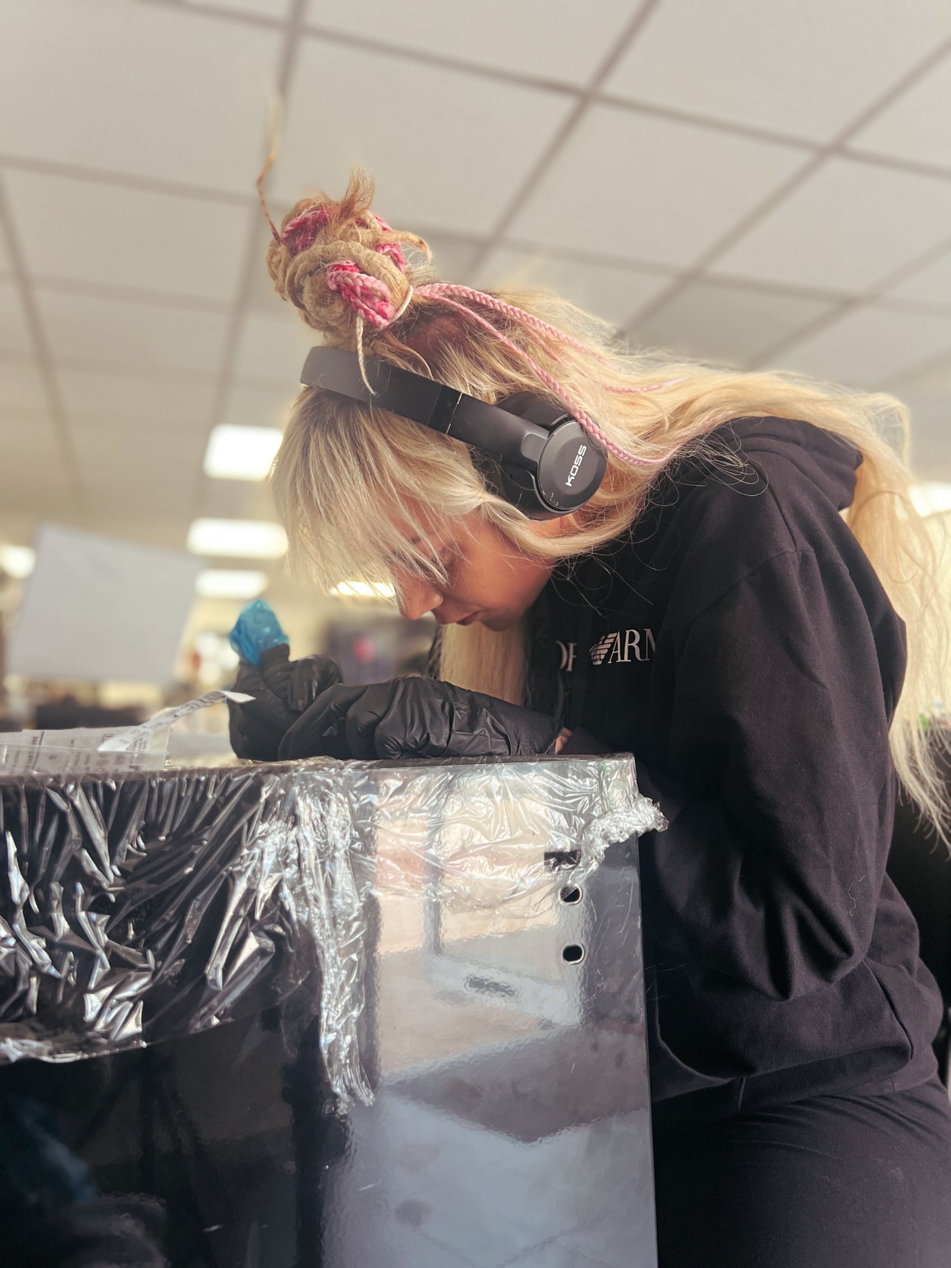 A person with blonde hair, wearing headphones, leaning over a covered surface, potentially working on a project.