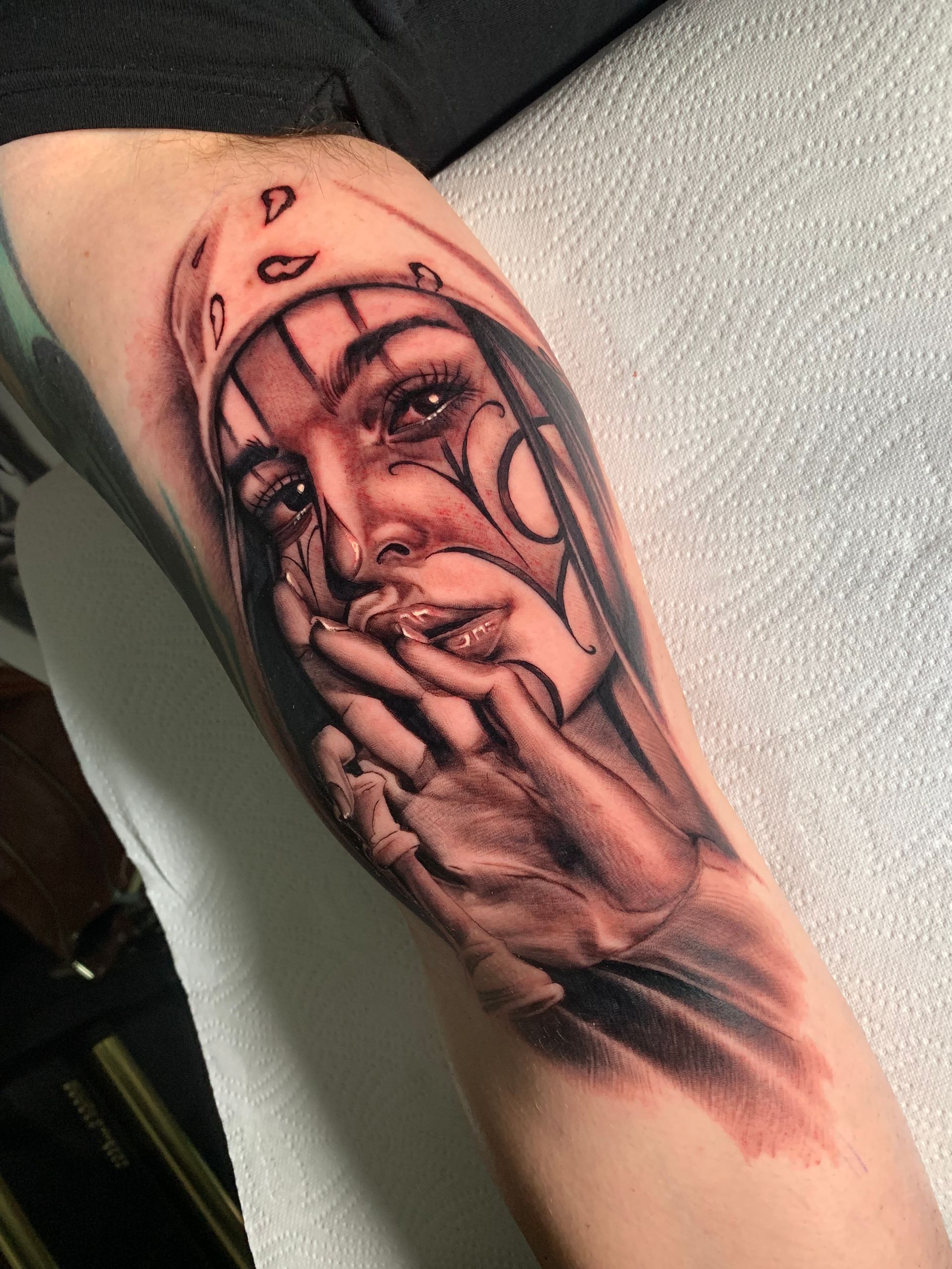 Black and white tattoo of a woman's face and hands praying. She wears a headscarf and has tears on her cheeks.