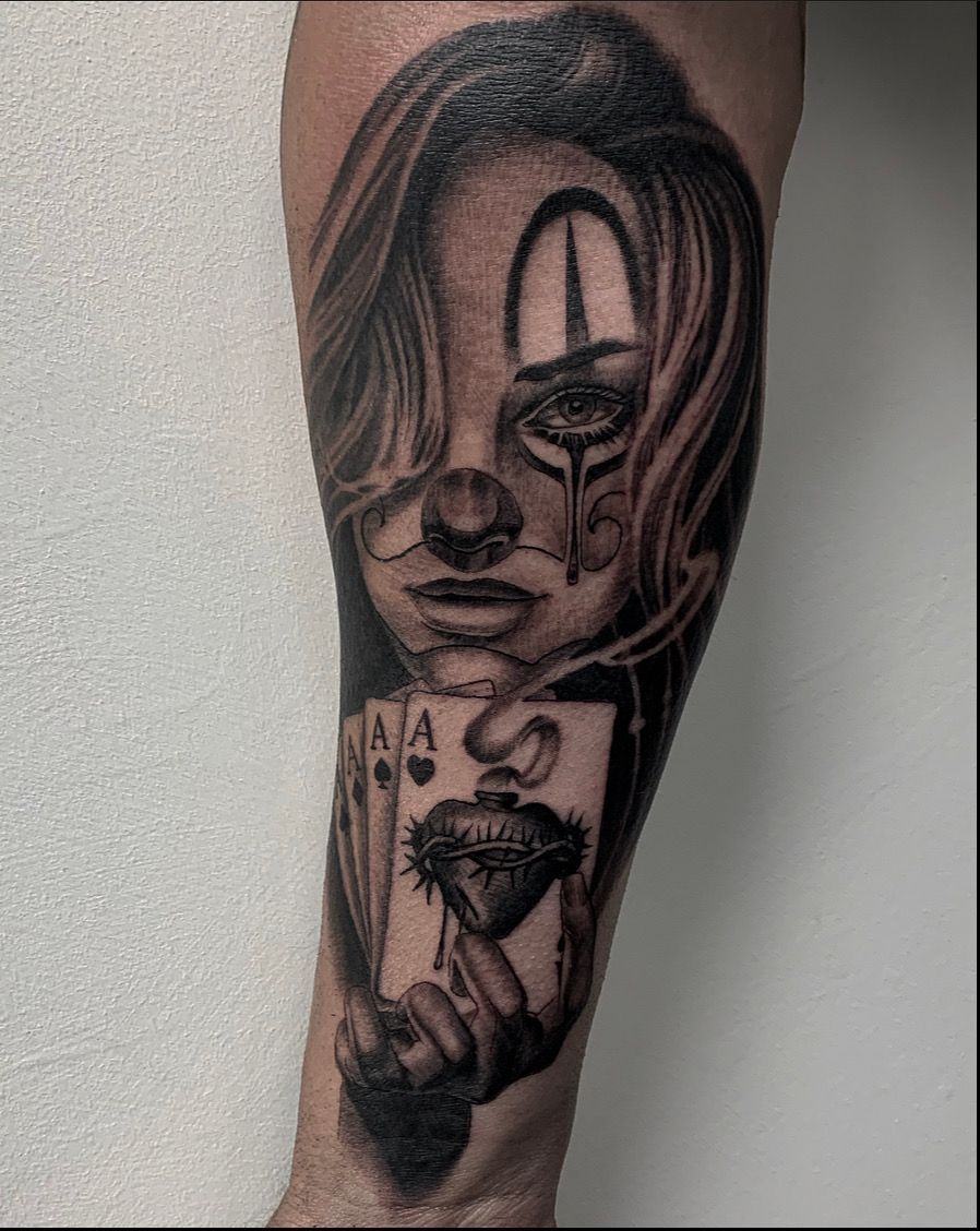 Black and white tattoo on an arm; a female clown with cards and a heart-shaped mouth.