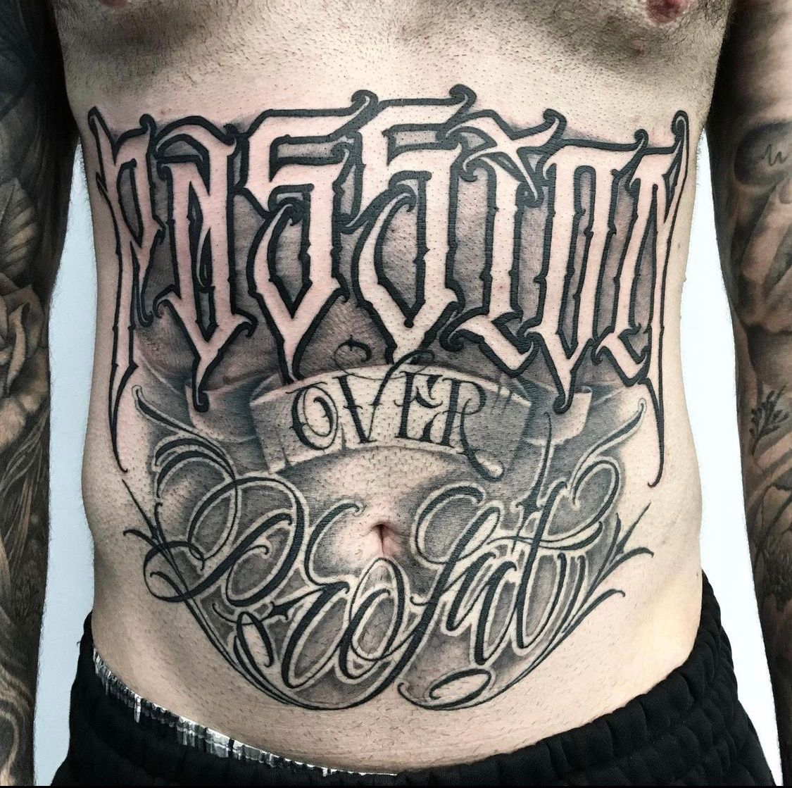 Tattoo on a person's stomach in gothic lettering that reads