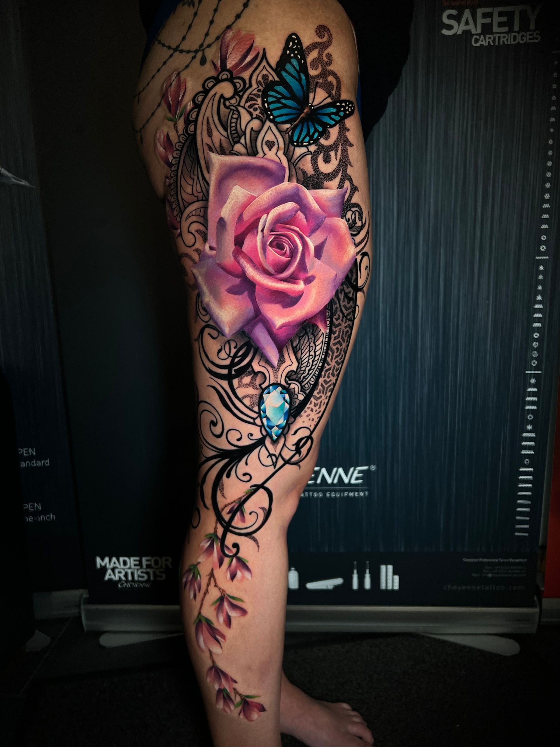 Rose and butterfly tattoo on a leg, featuring a vibrant pink rose, blue butterfly, and ornate black lace.