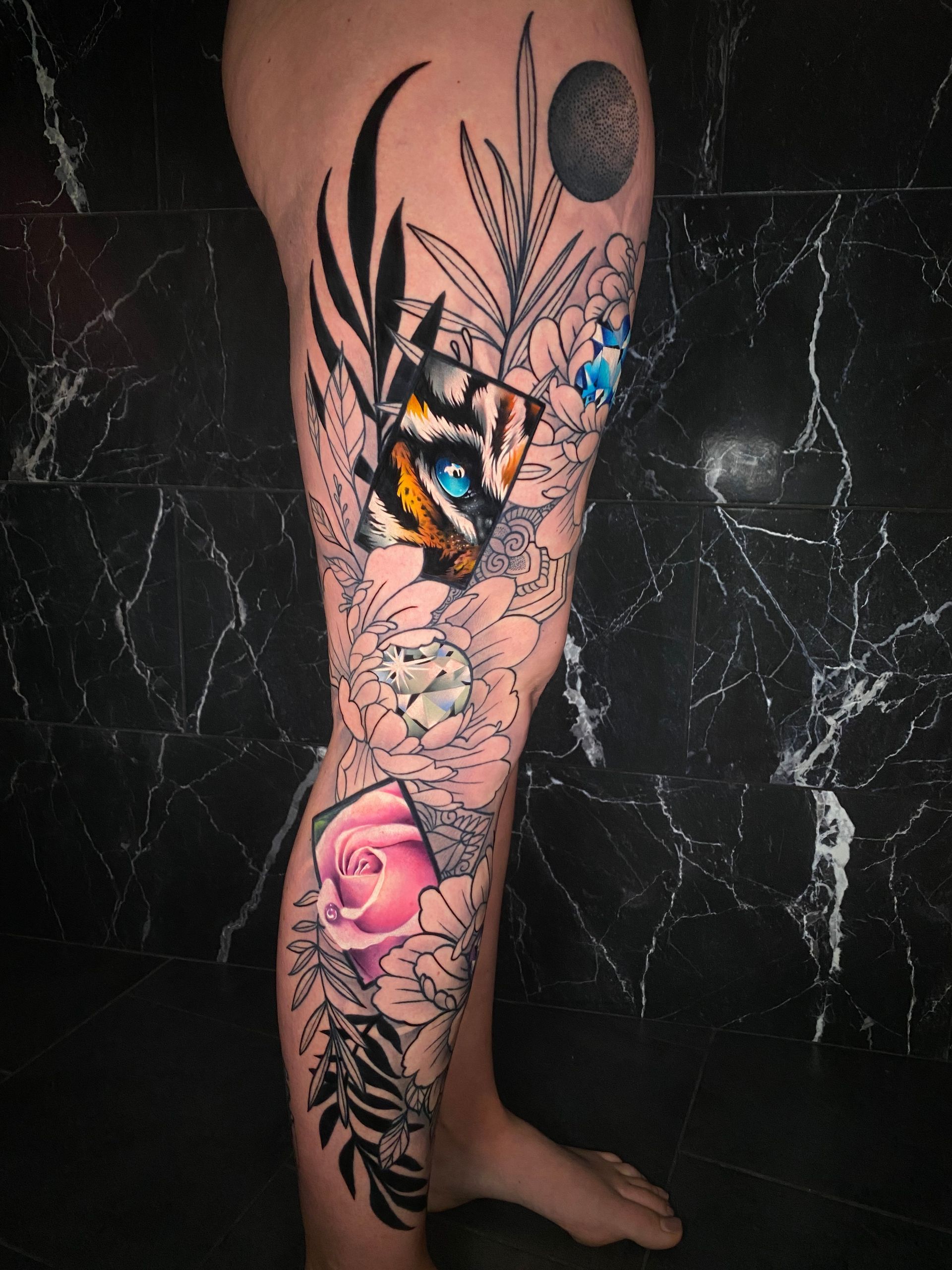 Tattoo of a tiger's face with colorful details, surrounded by floral elements on a leg. Black, white, blue, pink, and yellow color scheme.