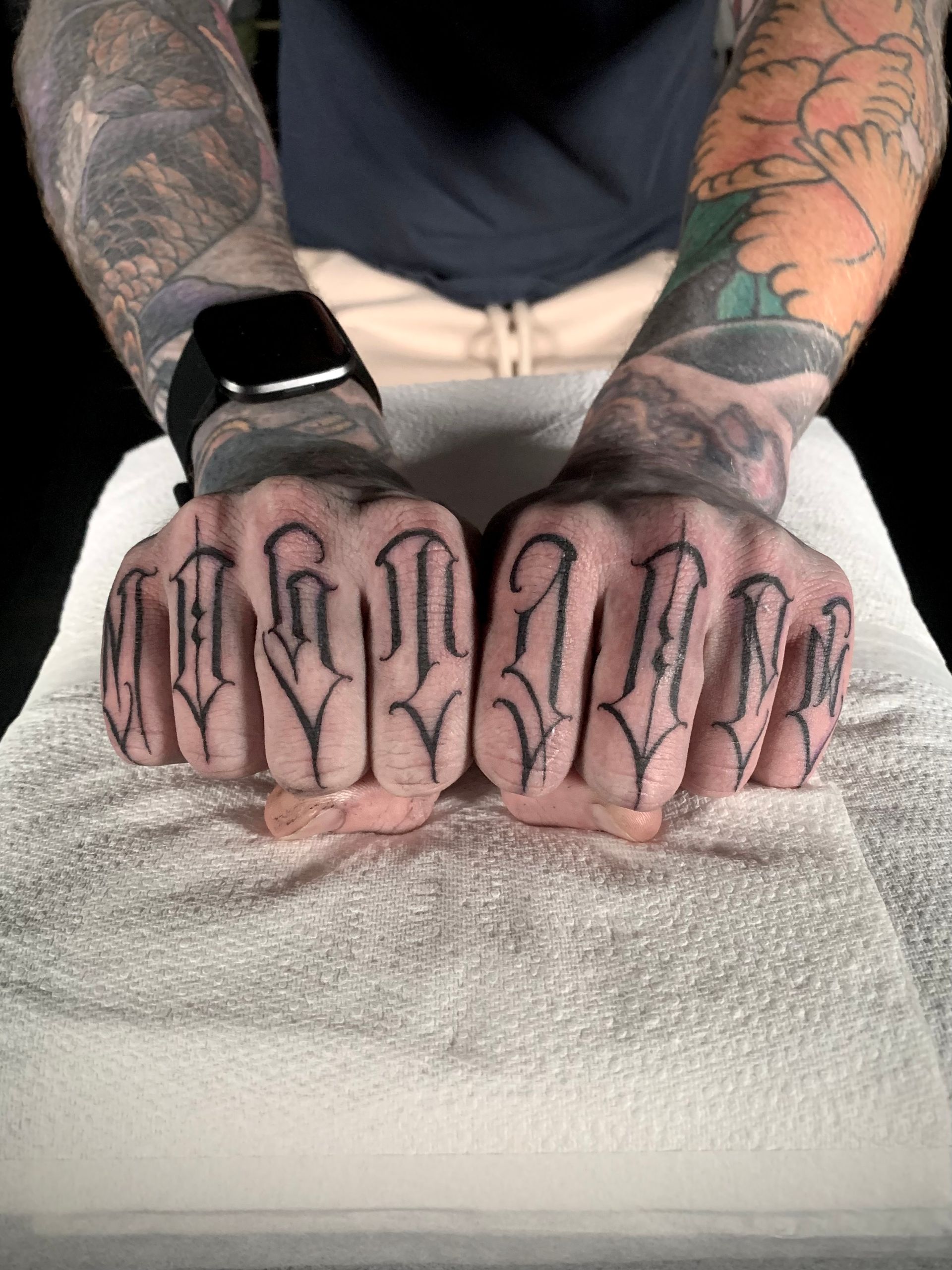 Hands with heavily tattooed knuckles, spelling out