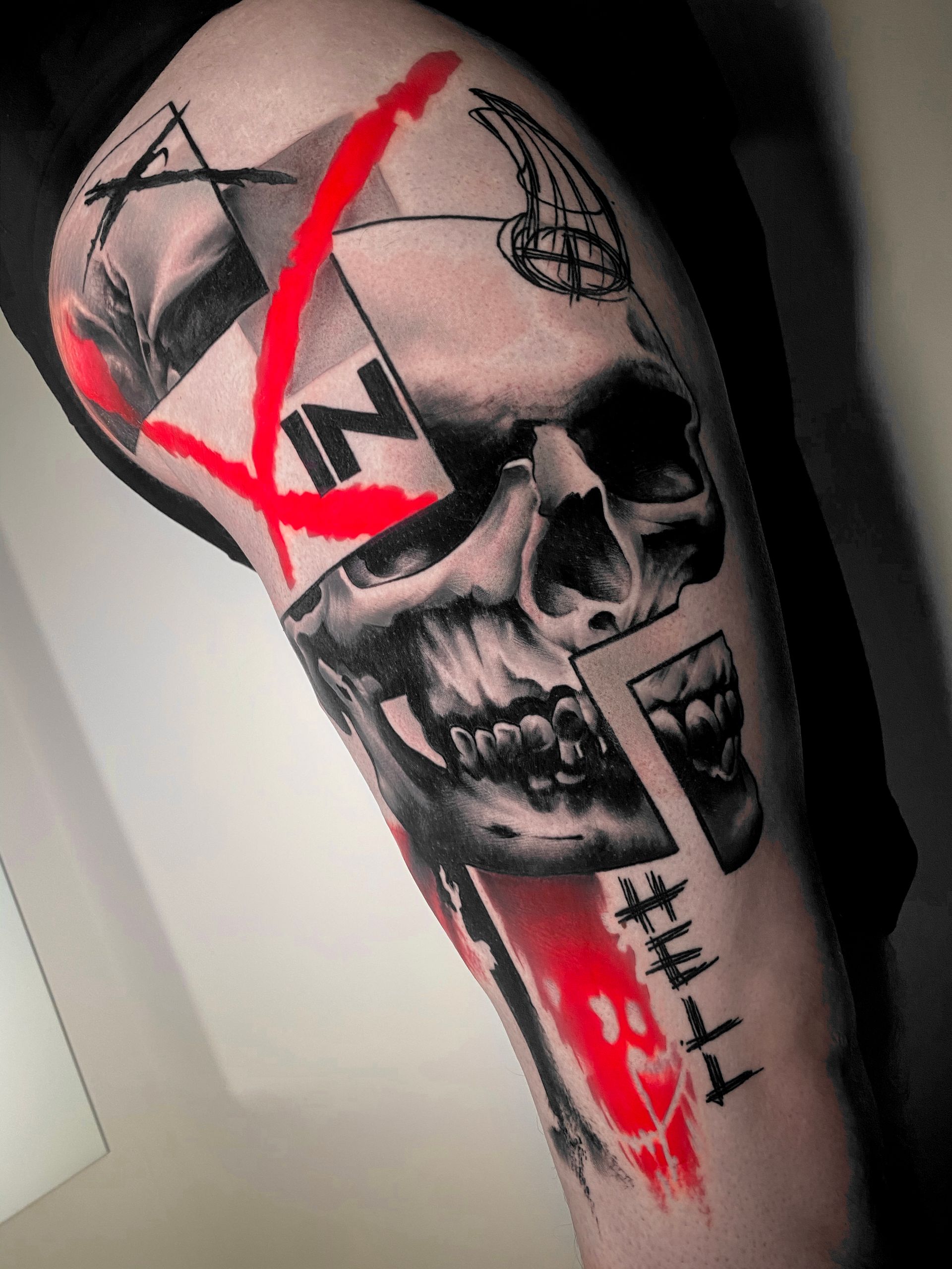 Black and red tattoo of a skull with abstract geometric shapes on an arm. A red slash is drawn across.