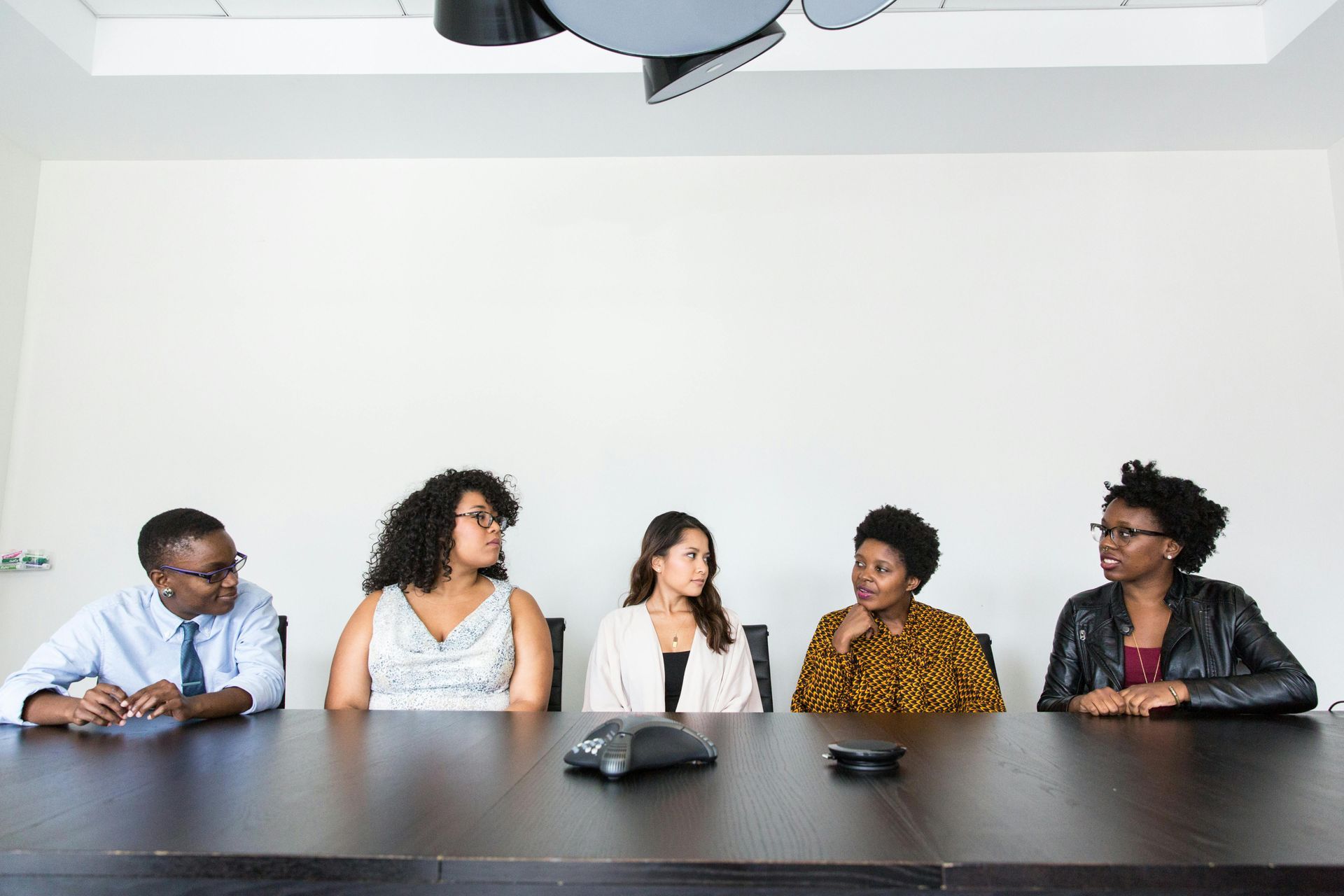 Five people sitting at a long conference table during a meeting in a bright, minimalist office.
