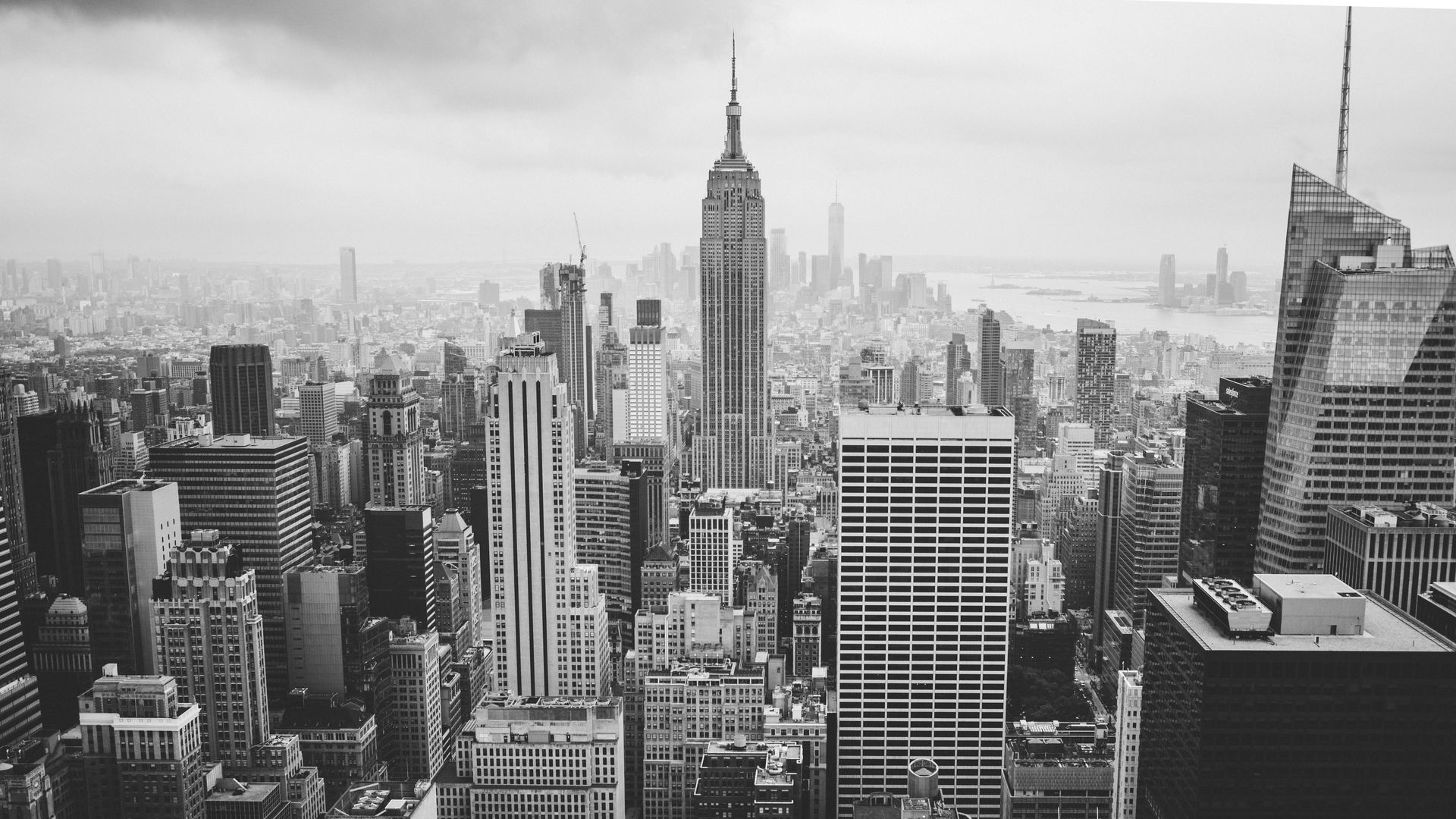 A high-angle, black-and-white cityscape view of New York City, dominated by the Empire State Building at center.