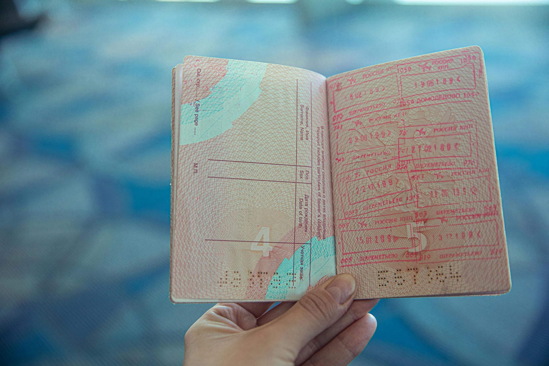 A hand holds an open passport with stamps on the pages against a blurred blue background.