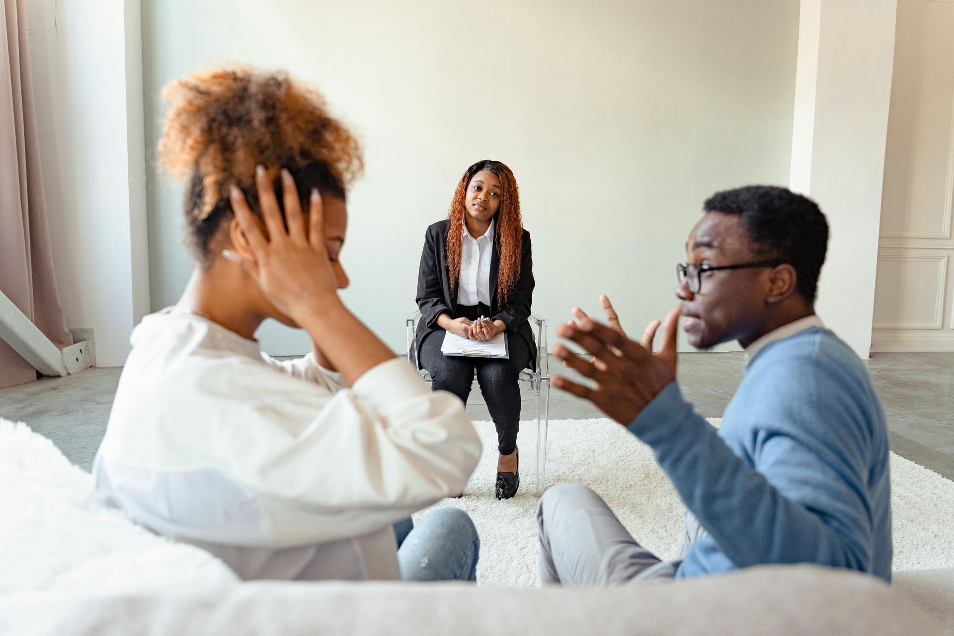 A person holds their head in distress while facing another person gesturing during a counseling session with a mediator.