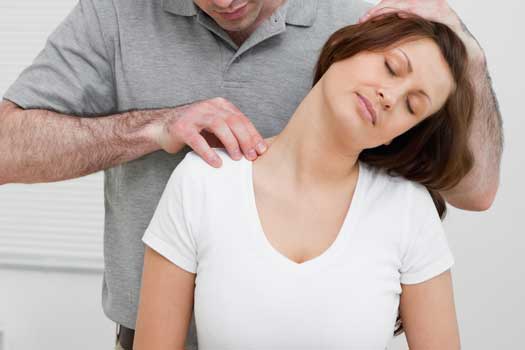 Serious osteopath palpating the trapezius of a woman in a room