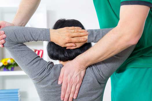 Serious osteopath palpating the trapezius of a woman in a room