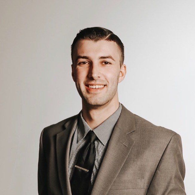 Man in a grey suit and tie smiling in front of a white background.