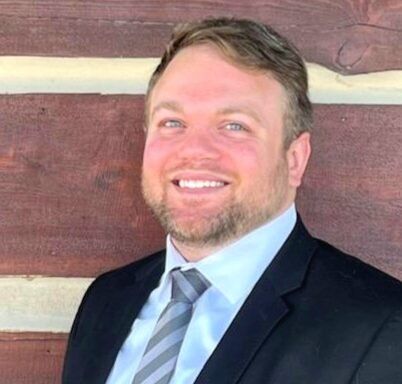 Man in suit smiles in front of a wood background.
