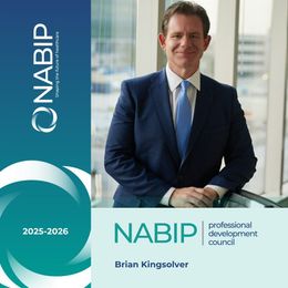 Brian Kingsolver in a suit smiles beside a window with the NABIP logo and 