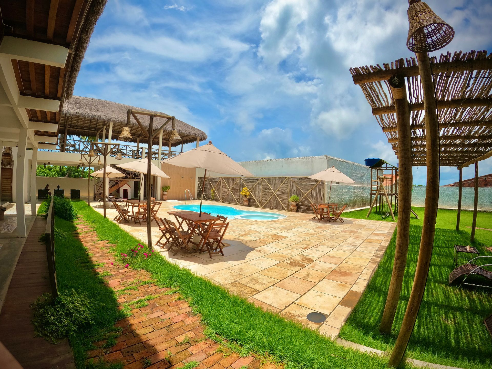 Um pátio com mesas, cadeiras e guarda-sóis em frente a uma piscina.