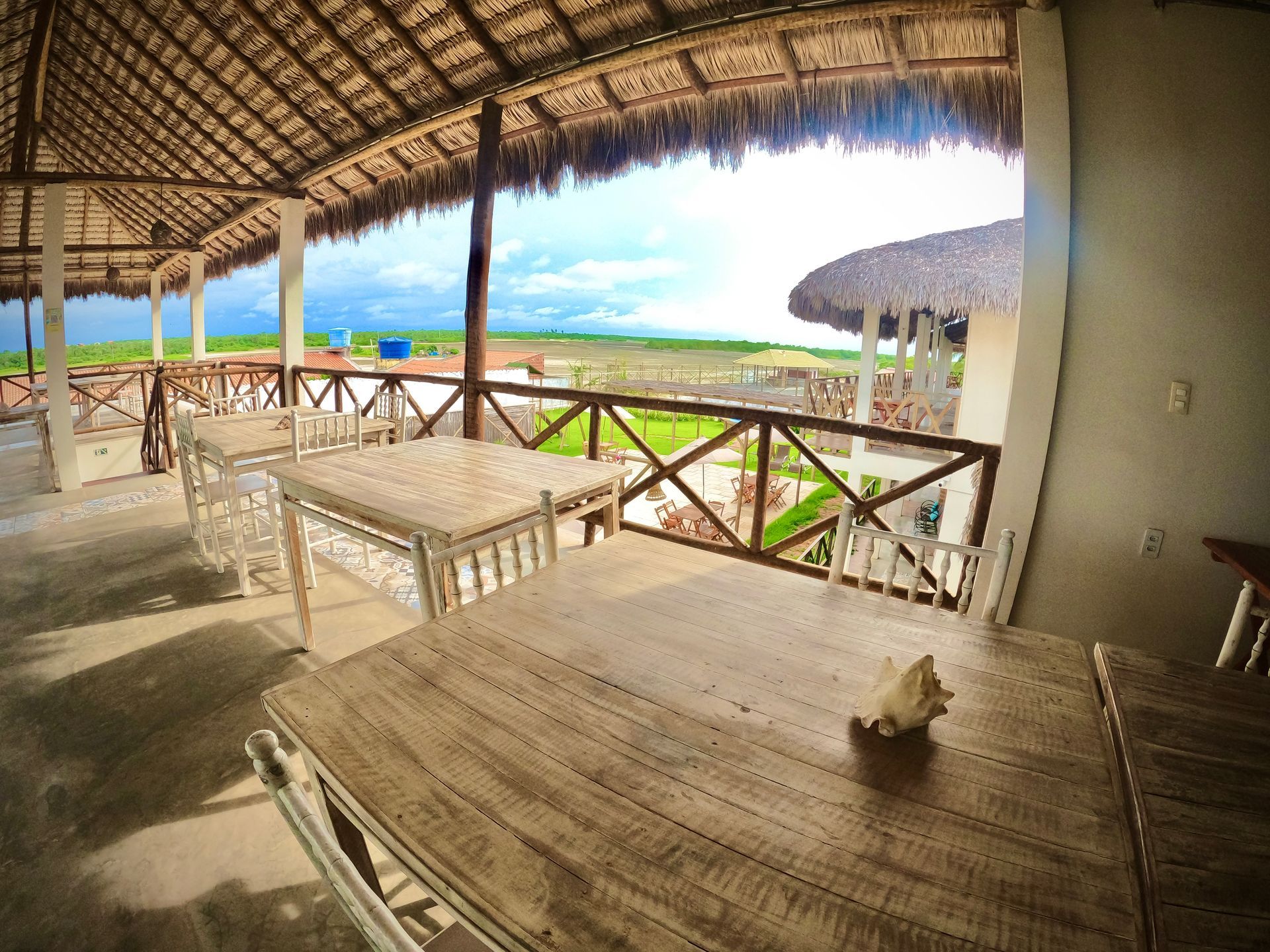 Uma mesa de madeira com uma concha em cima em um restaurante com telhado de palha.