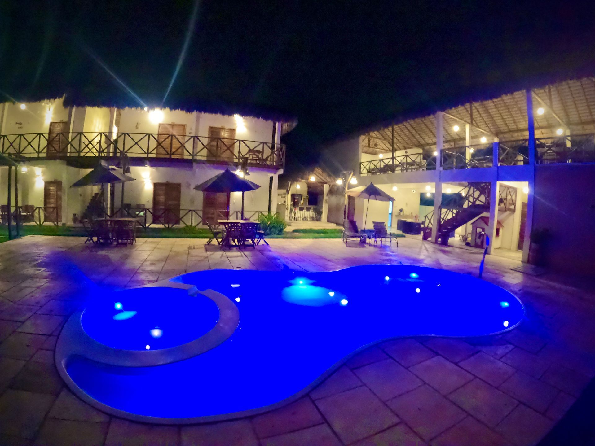 Uma grande piscina é iluminada à noite em frente a um hotel.