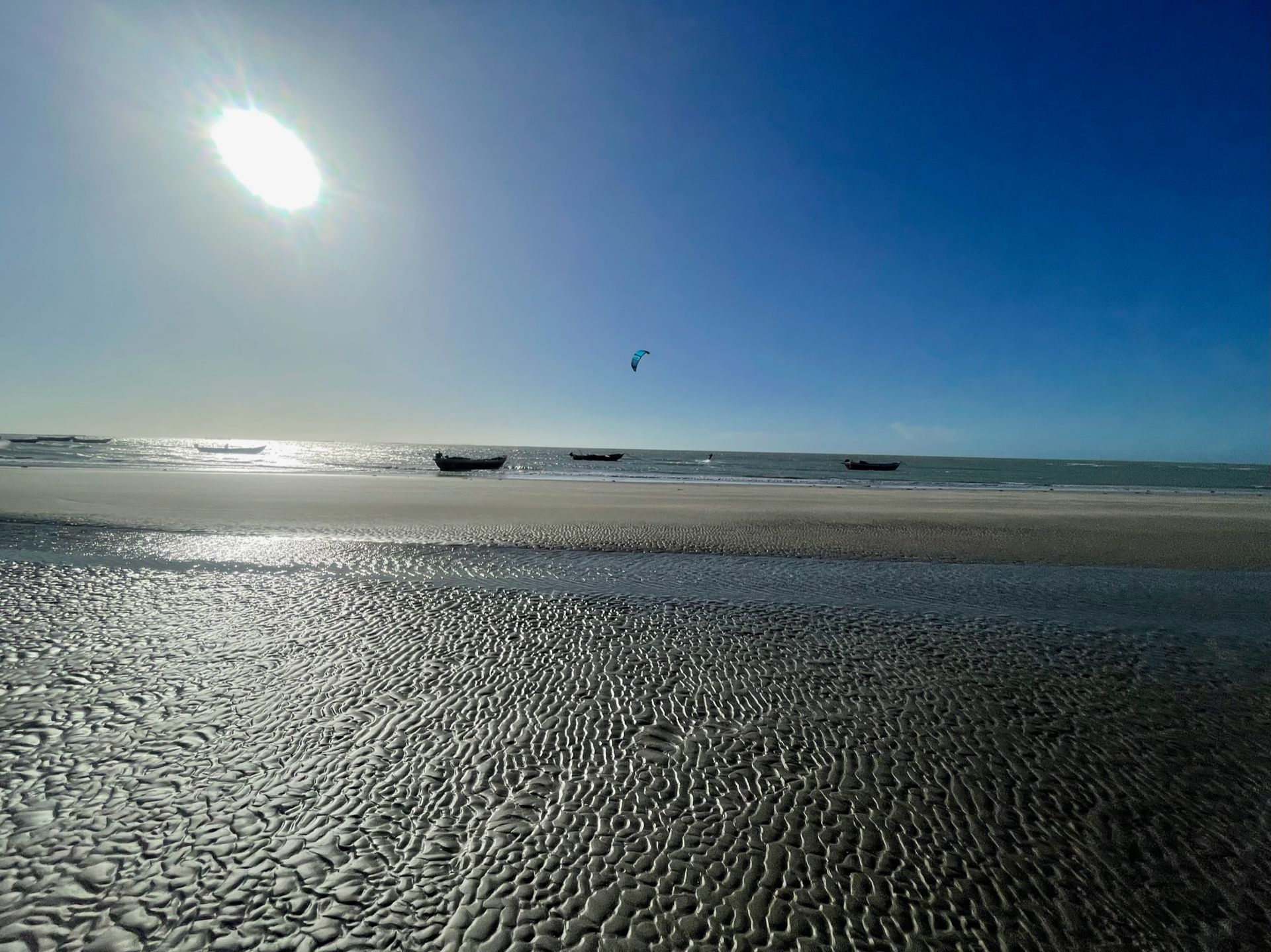 Uma praia de areia com um céu azul e o sol brilhando sobre ela