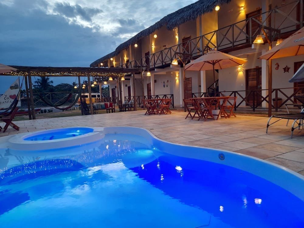 Uma grande piscina em frente a um hotel com mesas e cadeiras.