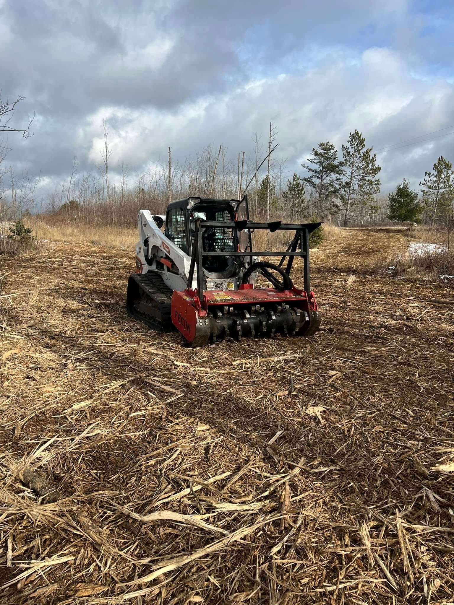 Bobcat skid-steer with a mulching head clearing brush in a field, under a cloudy sky.