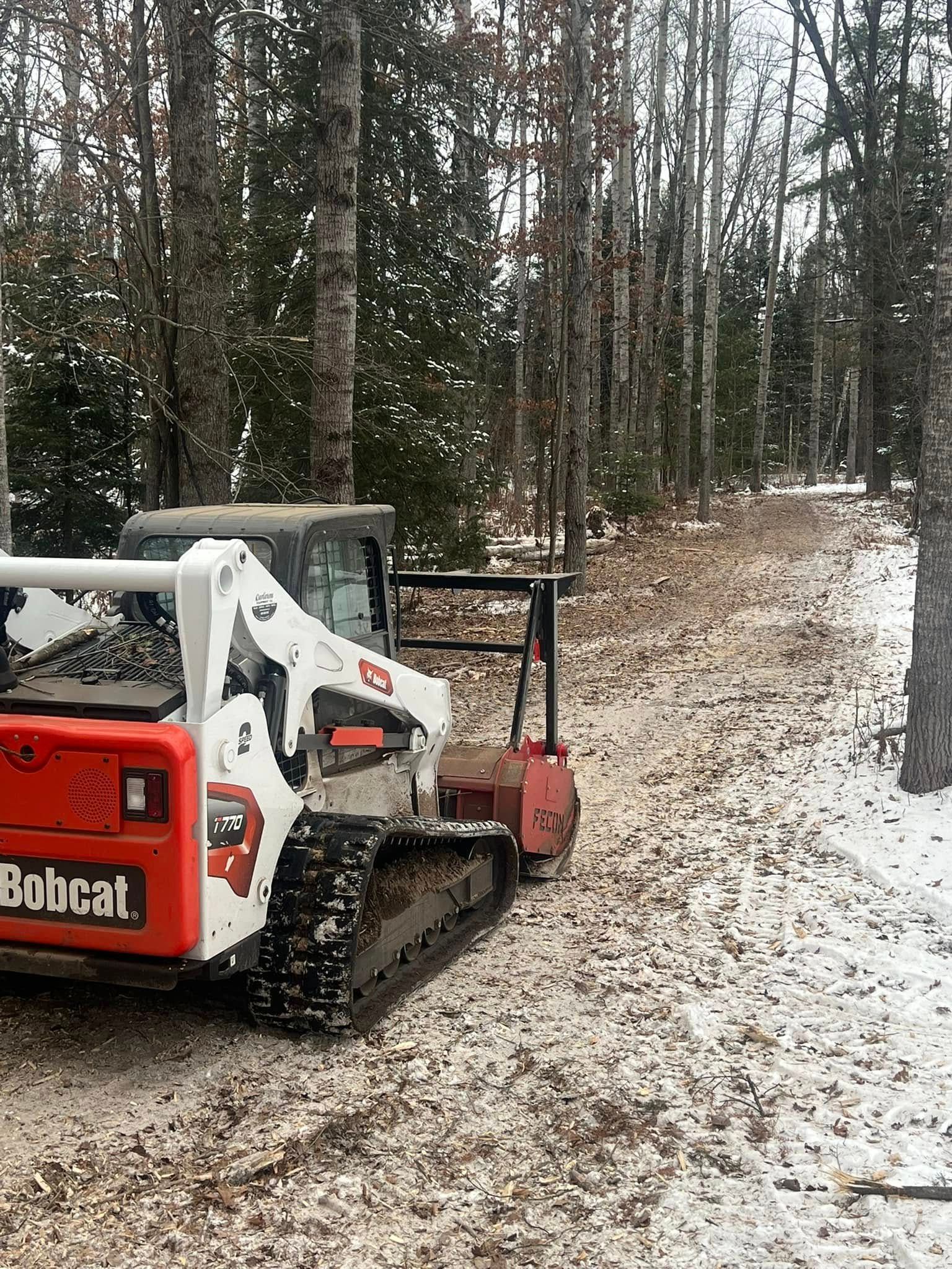 Bobcat tractor clearing a snowy wooded trail.