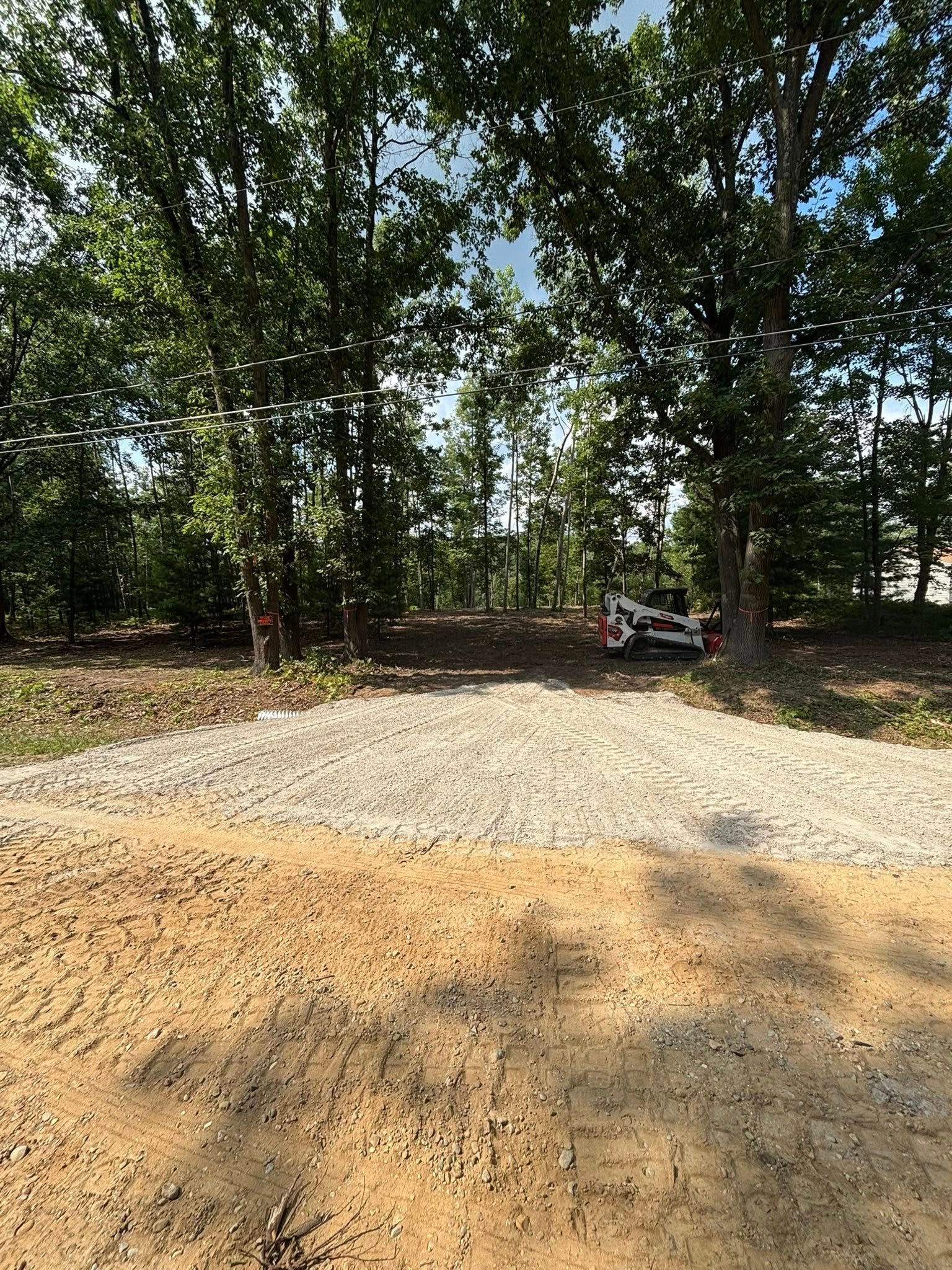 Dirt and gravel path leading into a wooded area, with a small excavator visible.