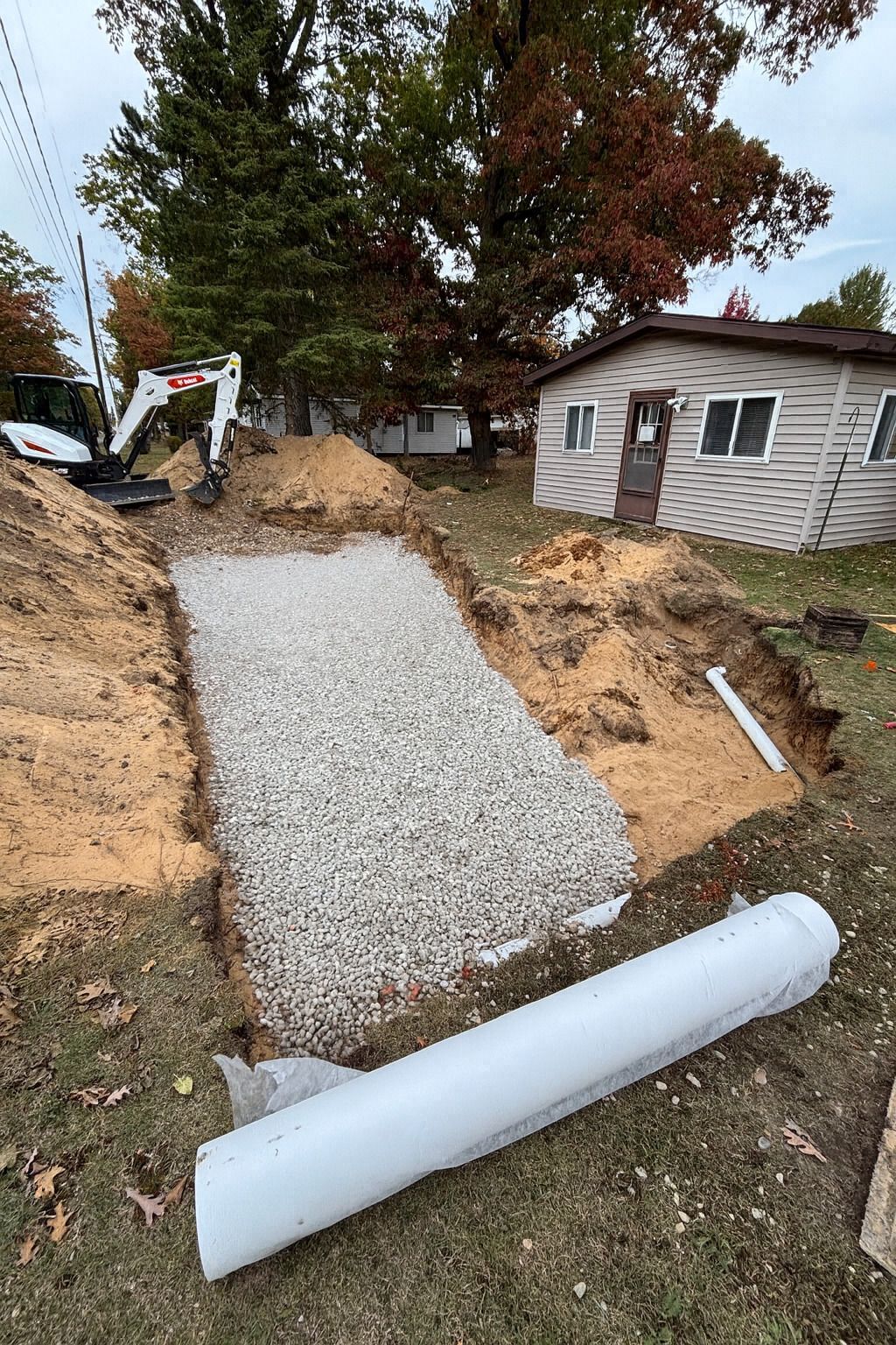 Excavated pit filled with gravel, prepared for installation next to a house. A small excavator is visible.