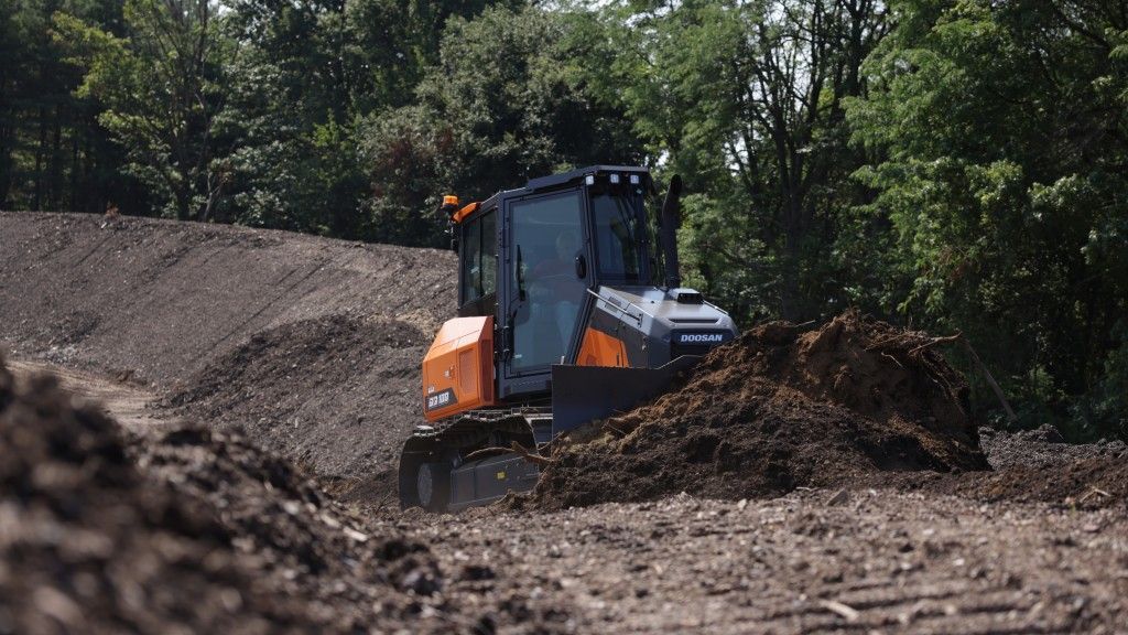Orange and black bulldozer moving dirt on a construction site with trees in the background.