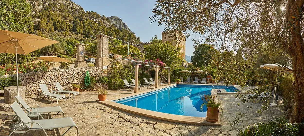 Una gran piscina rodeada de sillas y sombrillas en un jardín.