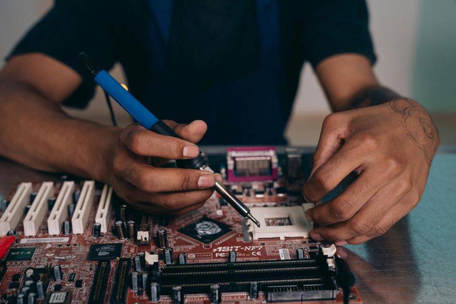 A man is soldering a motherboard with a soldering iron.