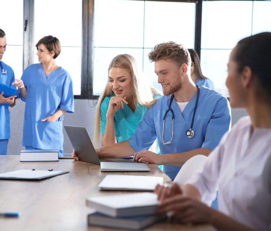 a group of doctors and nurses are sitting around a table looking at a laptop