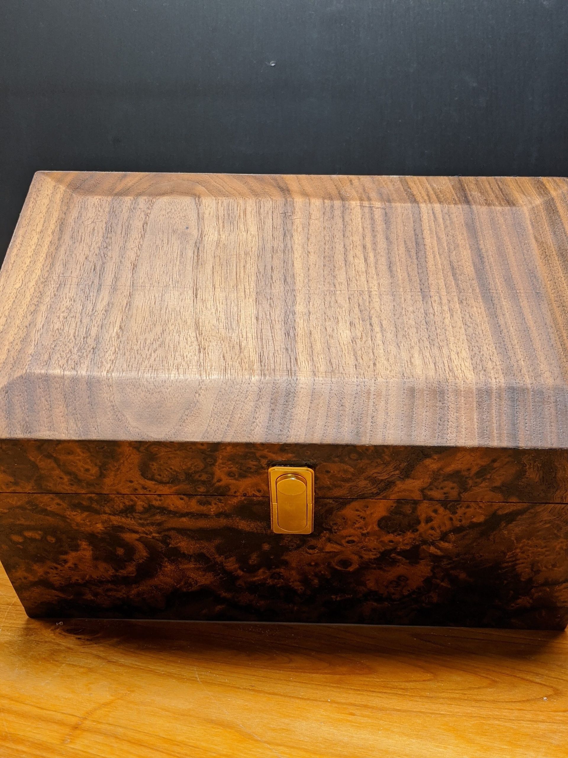 A wooden box with a gold lock is sitting on a wooden table.